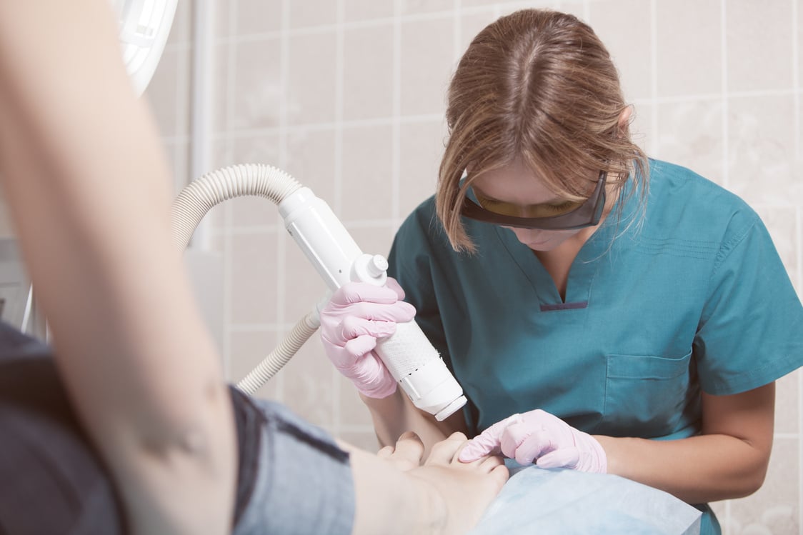 Female cosmetician doing foot therapy using laser